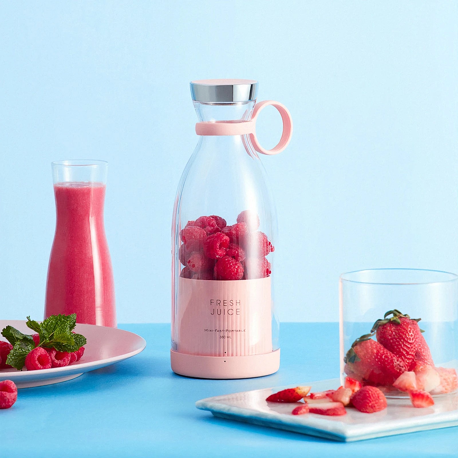 Pink juice bottle with raspberries, pink smoothie, and strawberries on a blue background