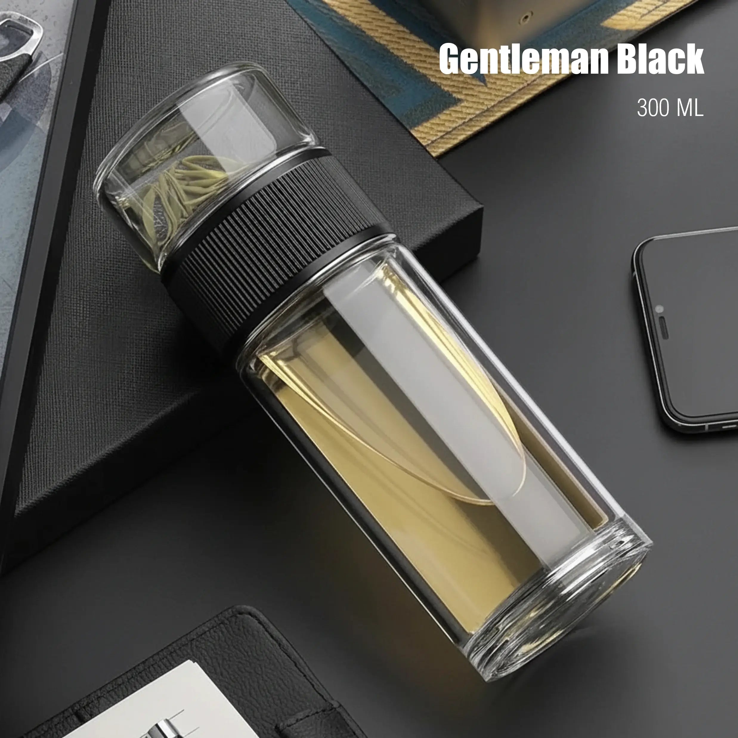 Clear glass water bottle with black lid on a dark surface, labeled 'Gentleman Black' and '300 ML'.