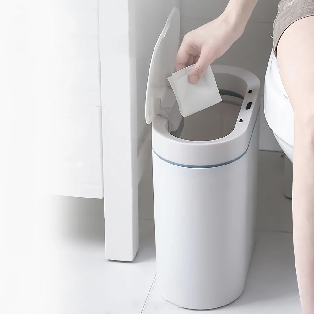 Person using a white trash can with a lid next to a toilet.
