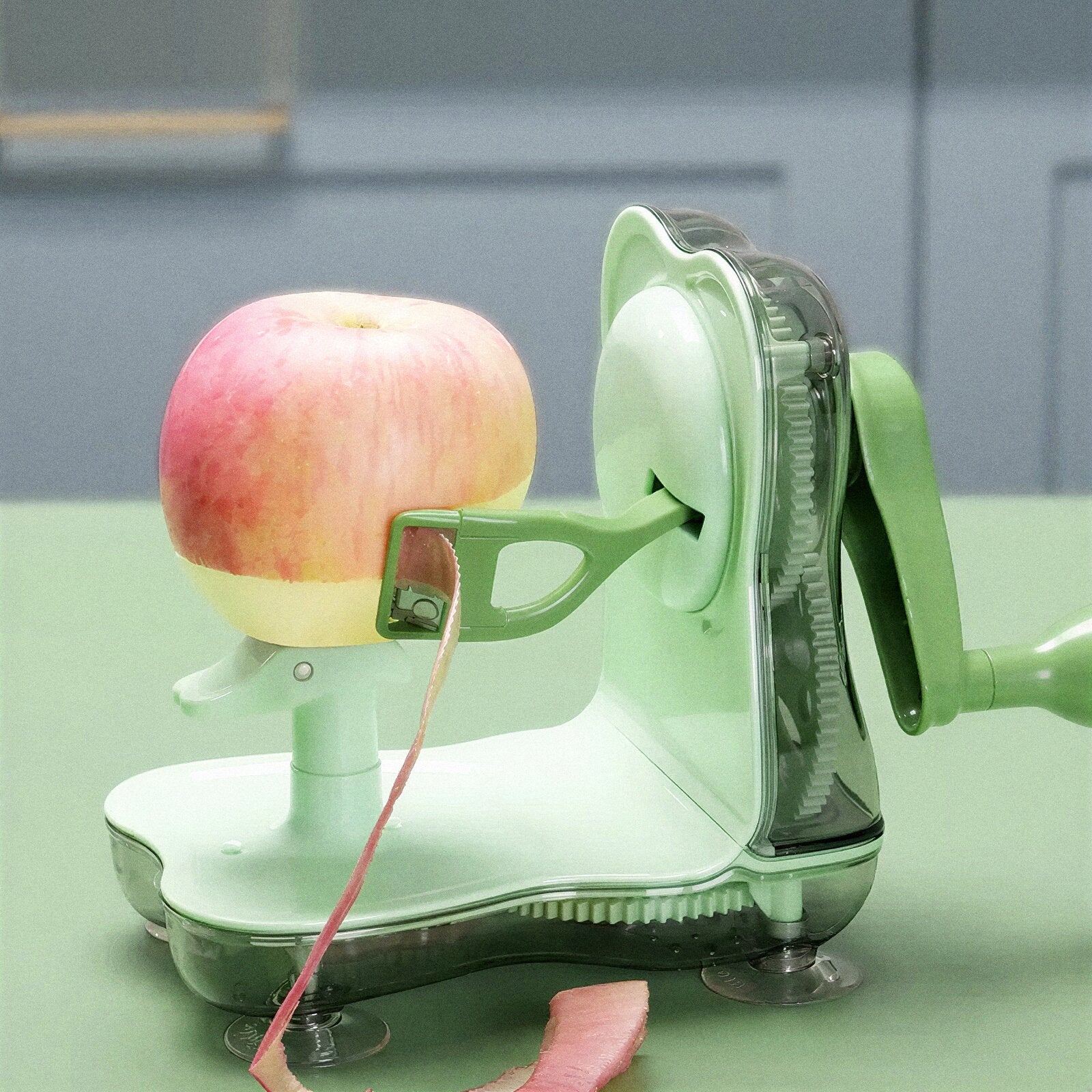 Green apple peeler with an apple being peeled on a green surface